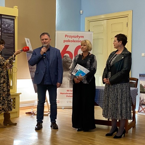 Powiększ obraz: Organizatorzy witający publiczność. W tle redaktor Katarzyna Kużel z Polskiego Radia Koszalin nagrywa wystąpienie.